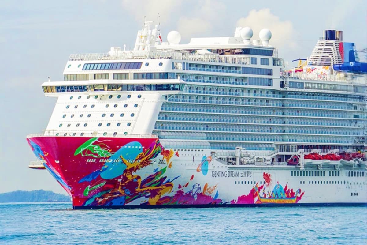 Genting Dream Singapore Roundtrip Cruise Large modern cruise ship with colorful pink and blue hull artwork sailing on blue ocean water