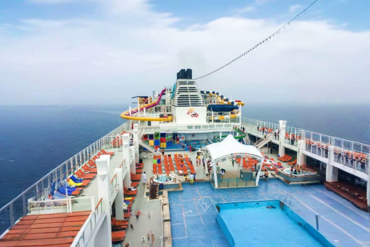 Genting Dream Singapore Roundtrip Cruise Aerial view of Genting Dream cruise ship deck with pools, loungers, water slides, and ocean scenery