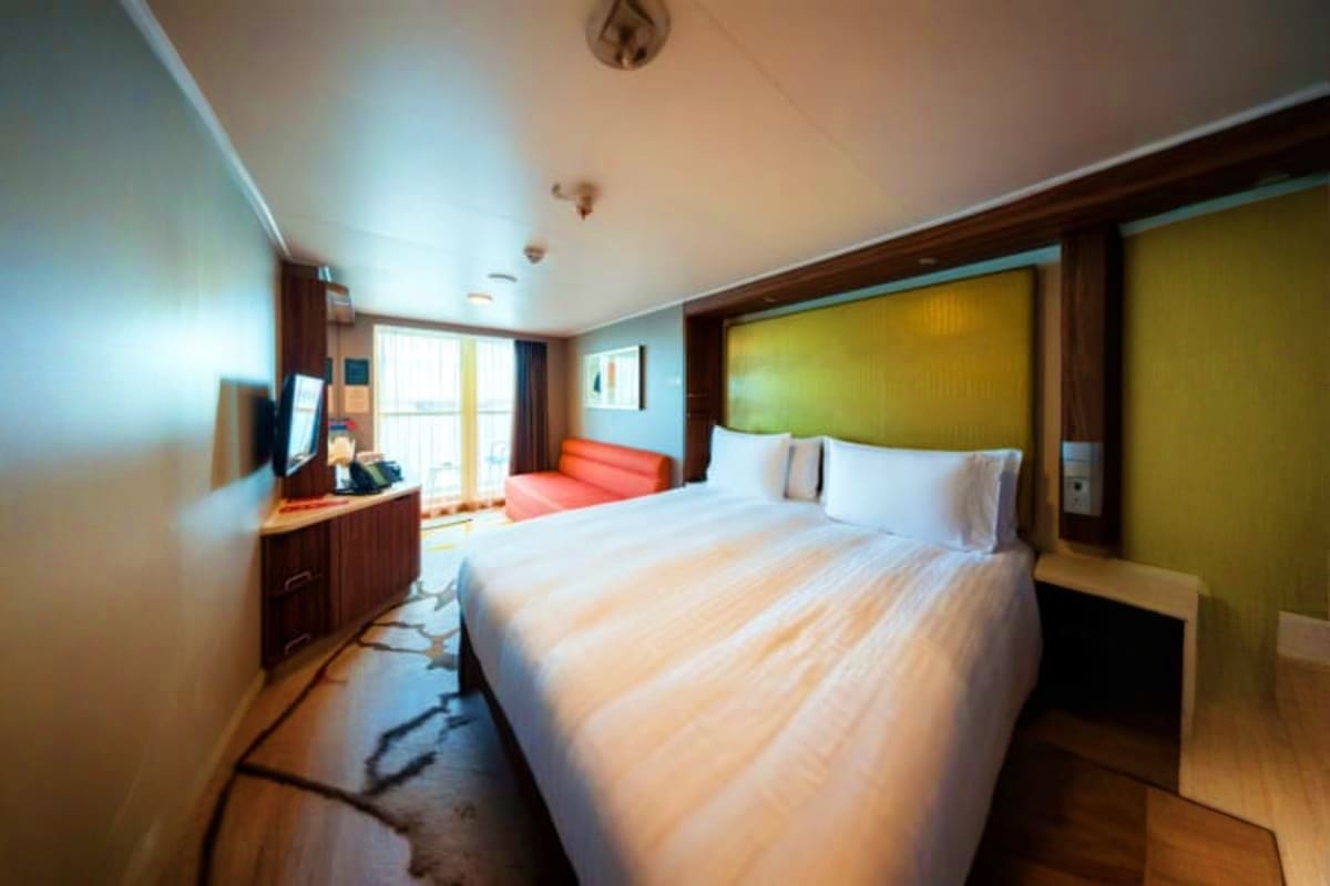 Genting Dream Singapore Roundtrip Cruise Modern cruise ship cabin with queen bed, olive green headboard, flat-screen TV, desk area, and ocean view balcony access