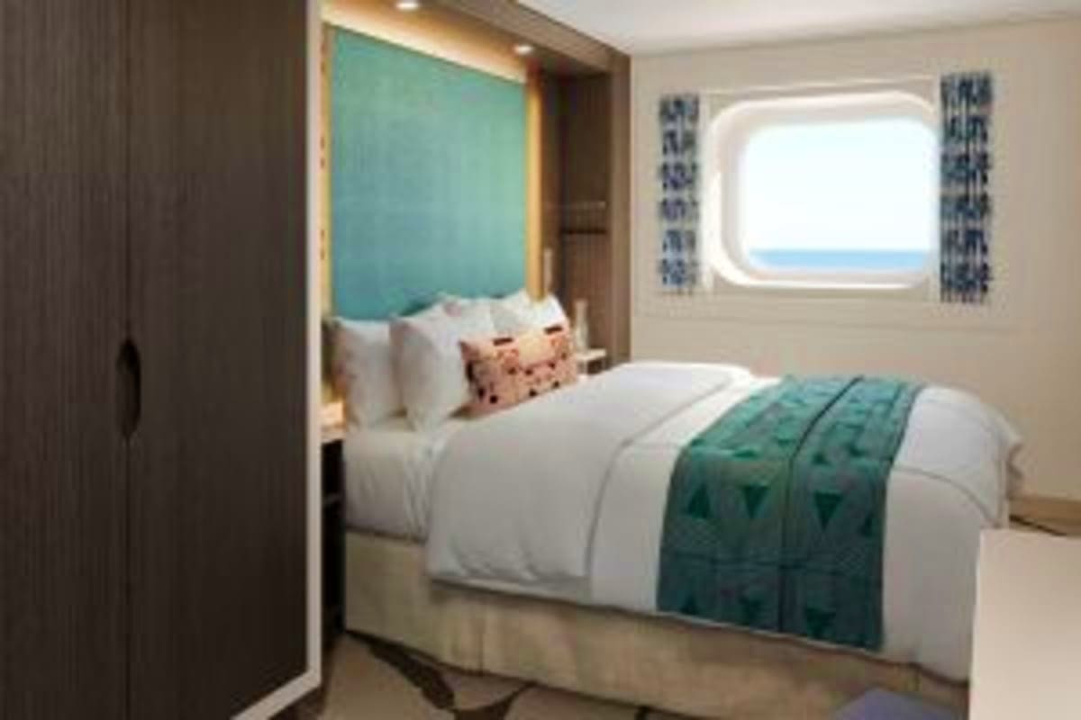 Modern cruise ship cabin with teal accent wall, white bedding with teal throw, porthole window overlooking ocean