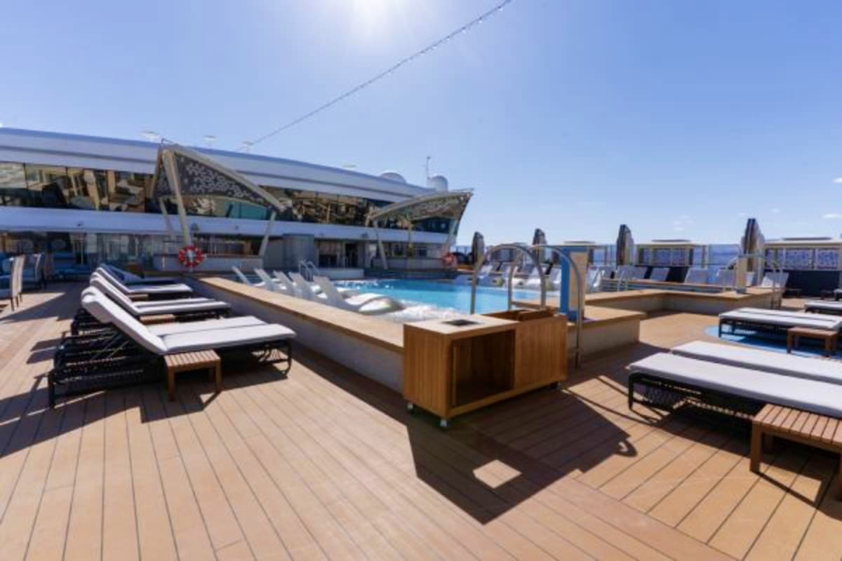 Cruise ship pool deck with lounge chairs, swimming pool, and ocean view on sunny day