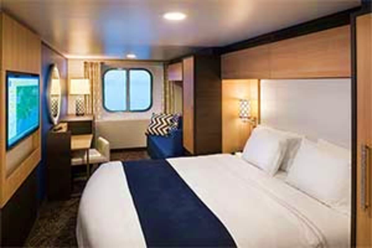 Spectrum of the Seas Vietnam Cruise Luxurious cruise ship cabin with queen bed, seating area, porthole windows, and modern wood and navy decor