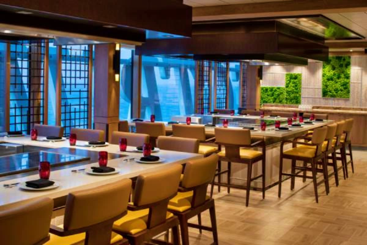 Spectrum of the Seas Asia Cruise Modern upscale dining room with tan chairs, white tables set with red centerpieces, floor-to-ceiling windows with ocean view,