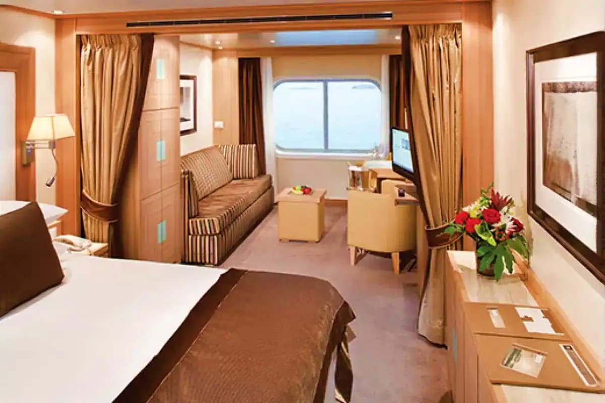 Seabourn Quest Aegean Gems Cruise Luxury cruise ship cabin interior with bed, sofa, ocean window, and elegant furnishings in warm tones
