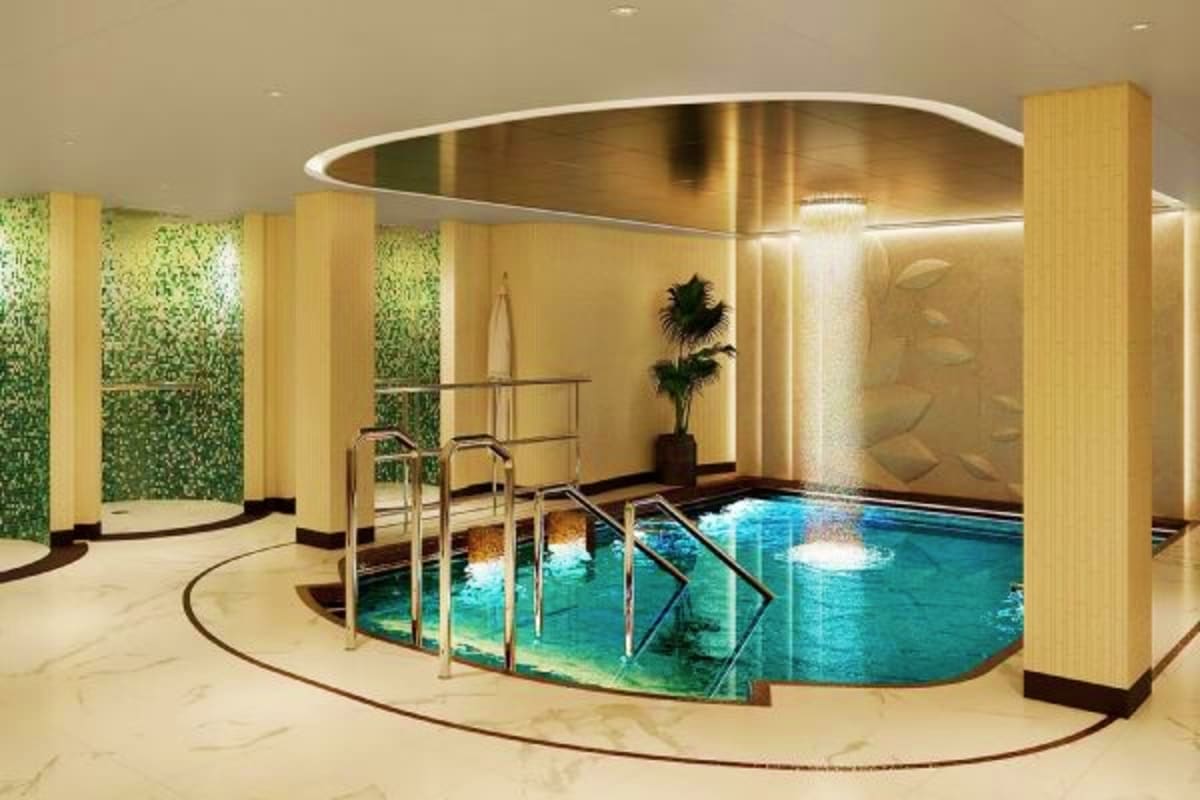 Sun Princess Greek Isles Escape Modern indoor swimming pool with turquoise water, metal railings, potted plant, and illuminated wooden columns in luxury crui