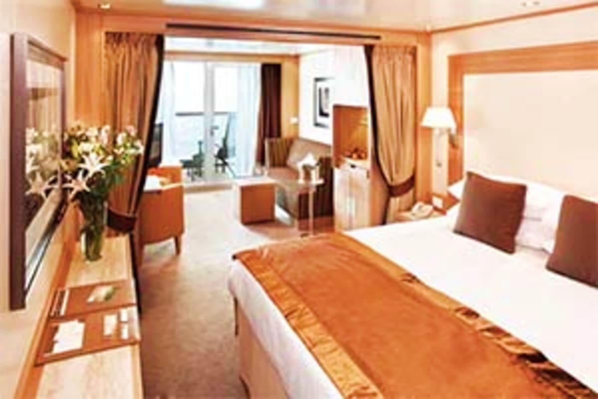Seabourn Quest Adriatic Greek Treasures Luxurious cruise ship suite with queen bed, sitting area, desk, windows with ocean views, warm wood furnishings and beige cur
