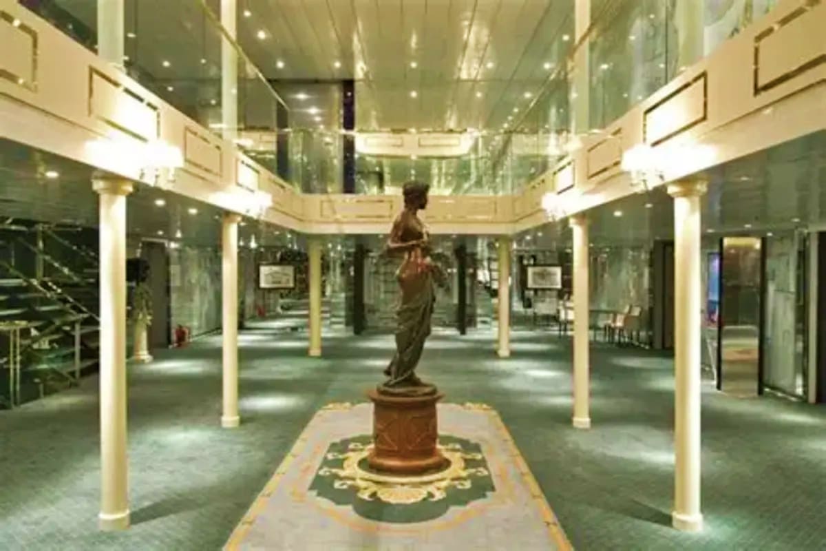 Costa Fascinosa Southern Europe Discovery Modern ship atrium with bronze statue on central pedestal, white columns, and glass railings overlooking multiple deck levels