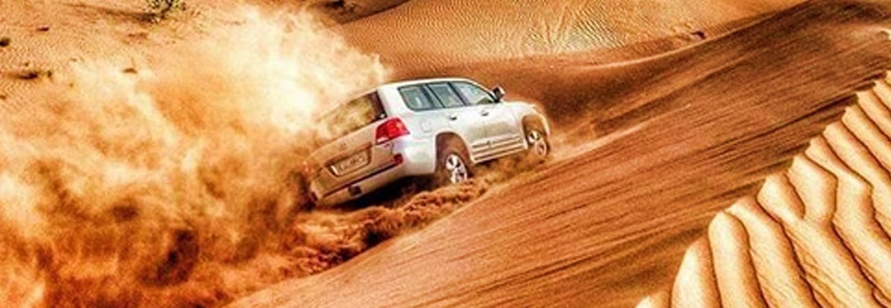 Sensational Ras Al Khaimah Getaway with Desert Safari White SUV driving down sandy desert dune creating dust cloud during desert safari adventure