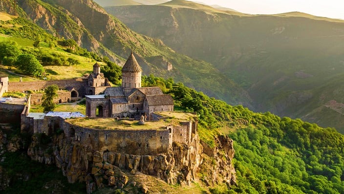 Ancient stone monastery perched on cliff overlooking lush green canyon valley in Armenia