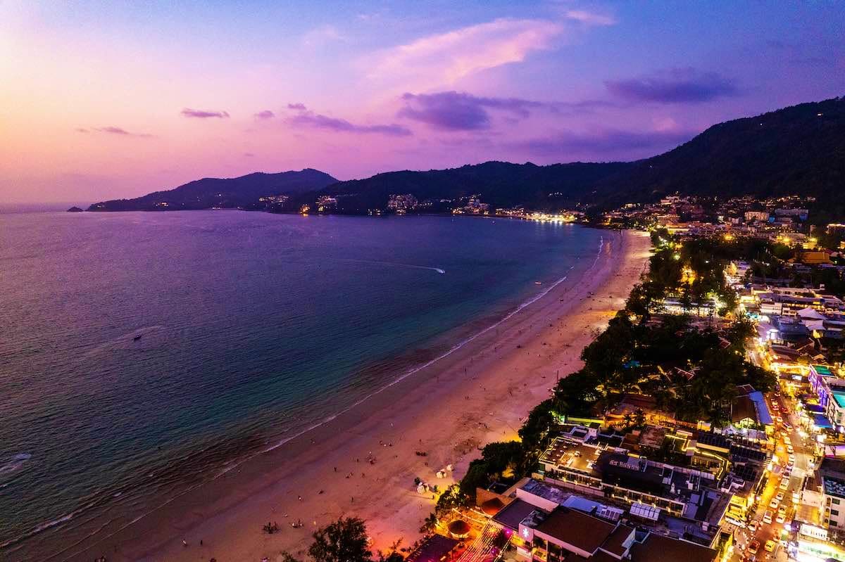 Scenic twilight view of Pattaya beach with illuminated coastal town, mountains, and calm bay at dusk
