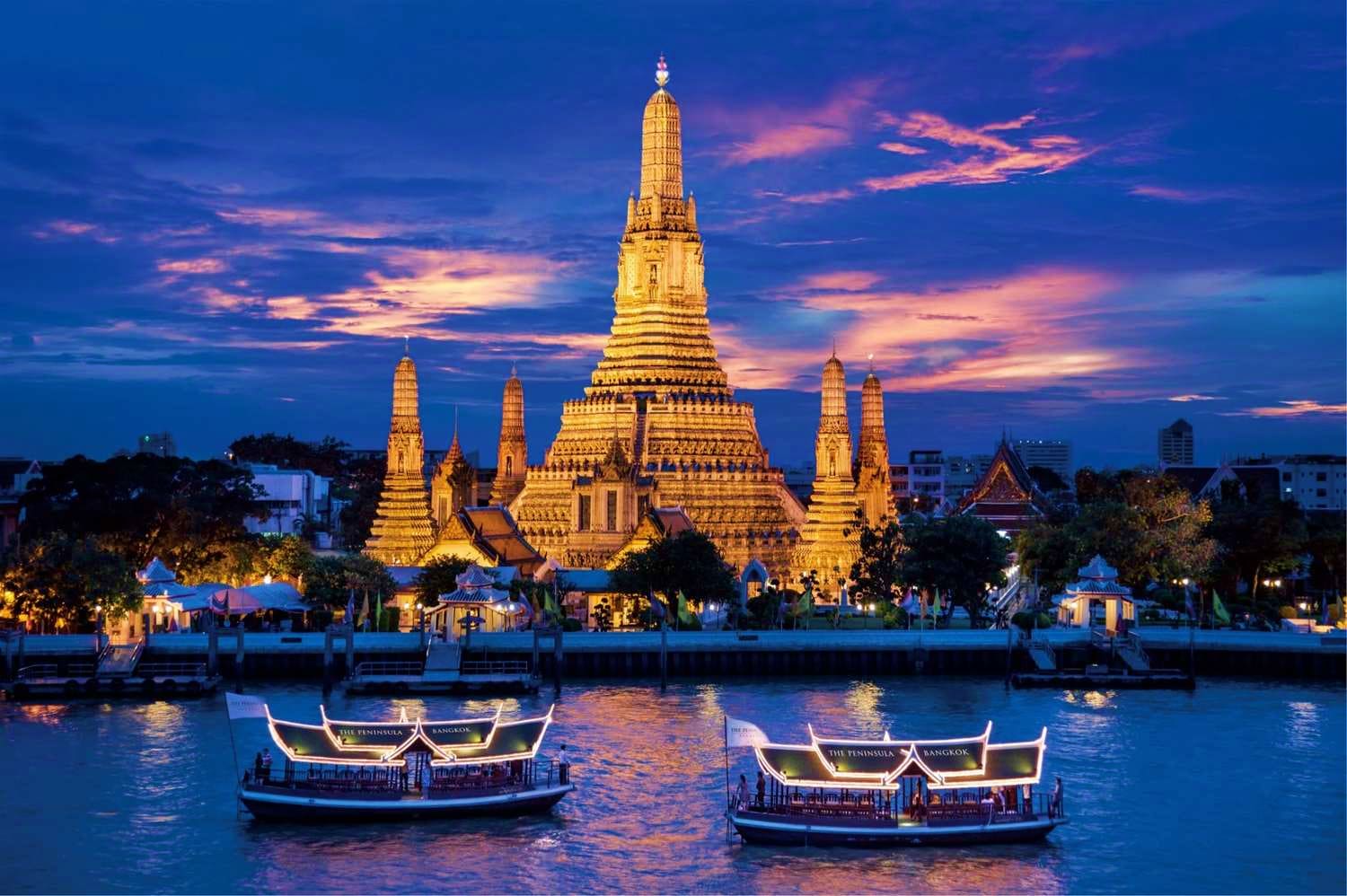 Wat Arun illuminated at dusk with traditional long-tail boats on the Chao Phraya River in Bangkok, Thailand