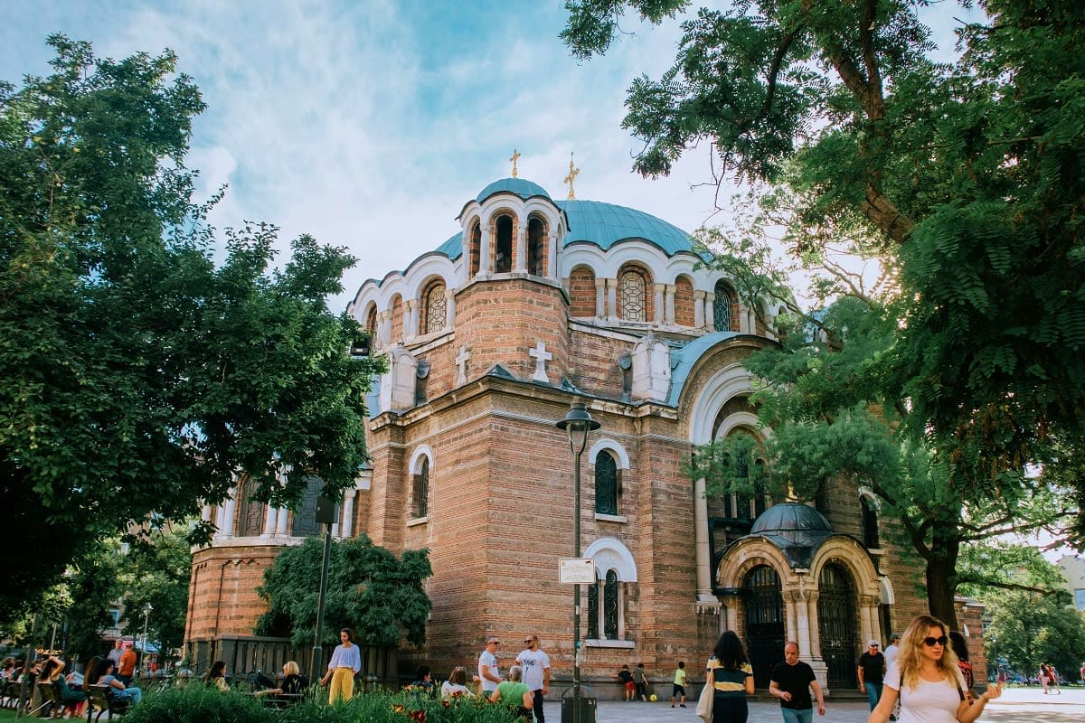 Sofia to Varna Cultural Trail Orthodox cathedral with blue domes and brick facade surrounded by green trees, visitors walking in plaza