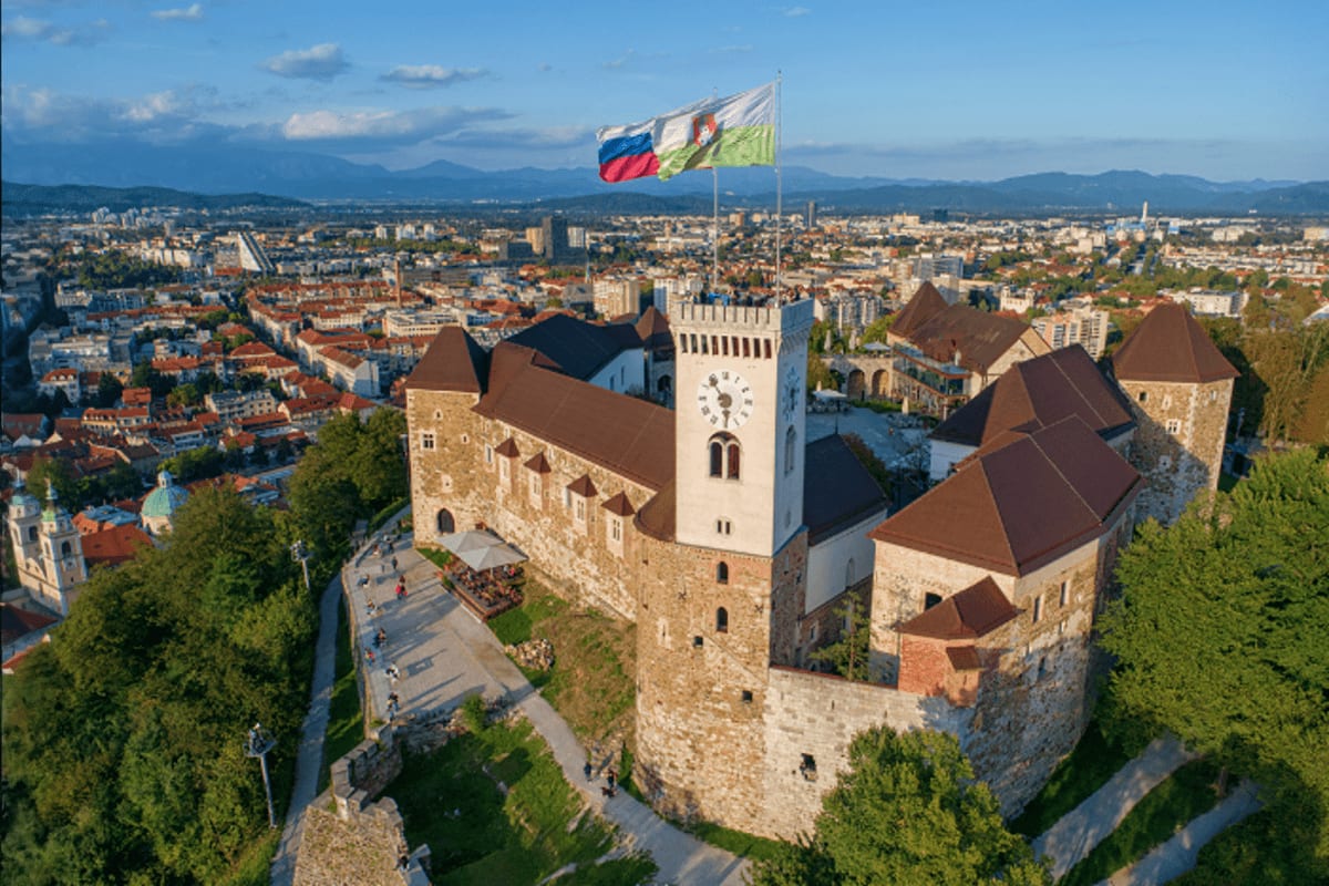 Aerial view of Ljubljana Castle with Slovenian flag, surrounded by the city skyline and mountains in the distance