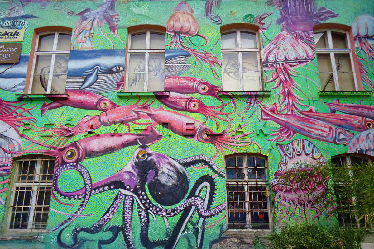 Colorful street art mural on building facade featuring whales, squid, jellyfish and sea creatures in pink and purple on brigh