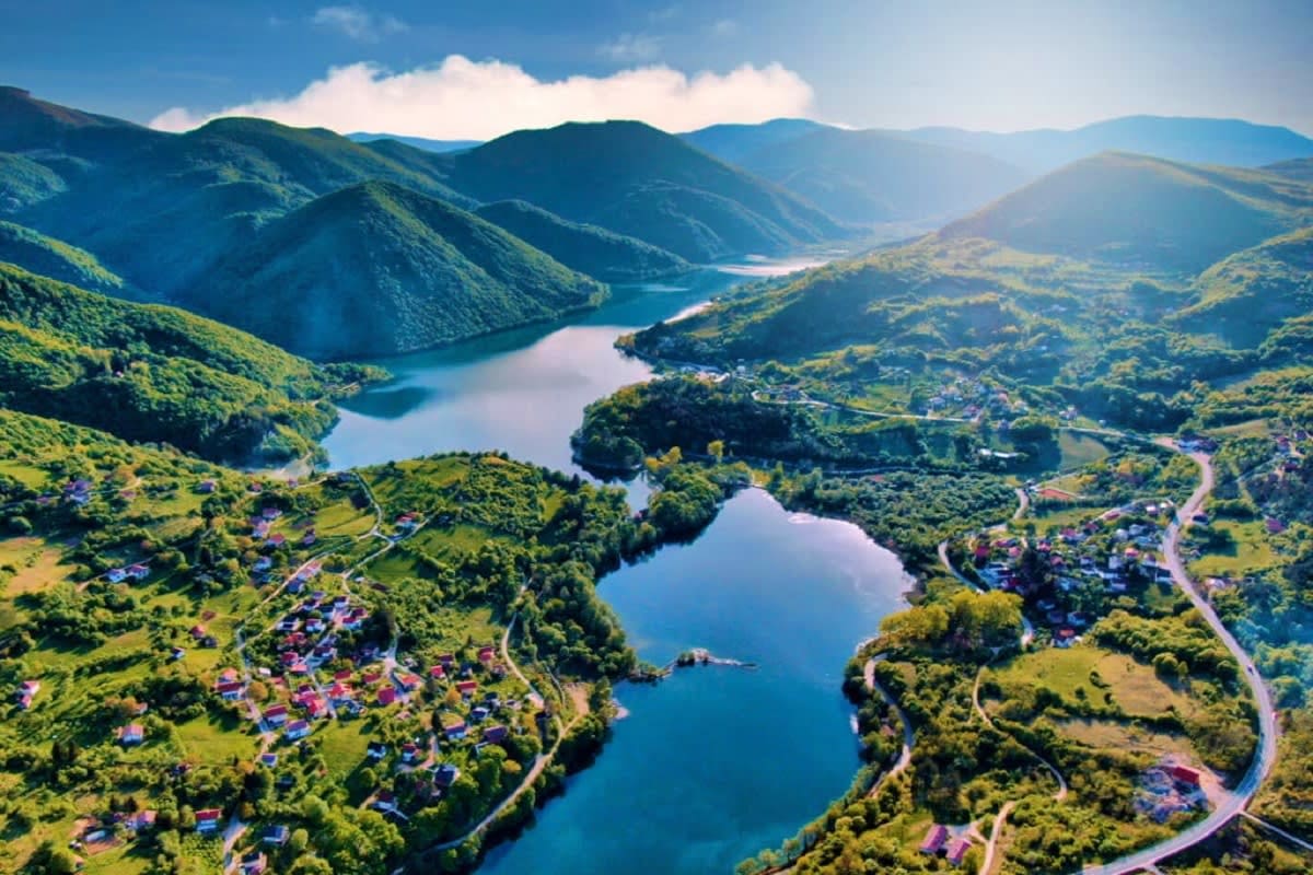 Aerial view of turquoise lakes surrounded by green mountains, forests, and scattered villages in Bosnia and Herzegovina