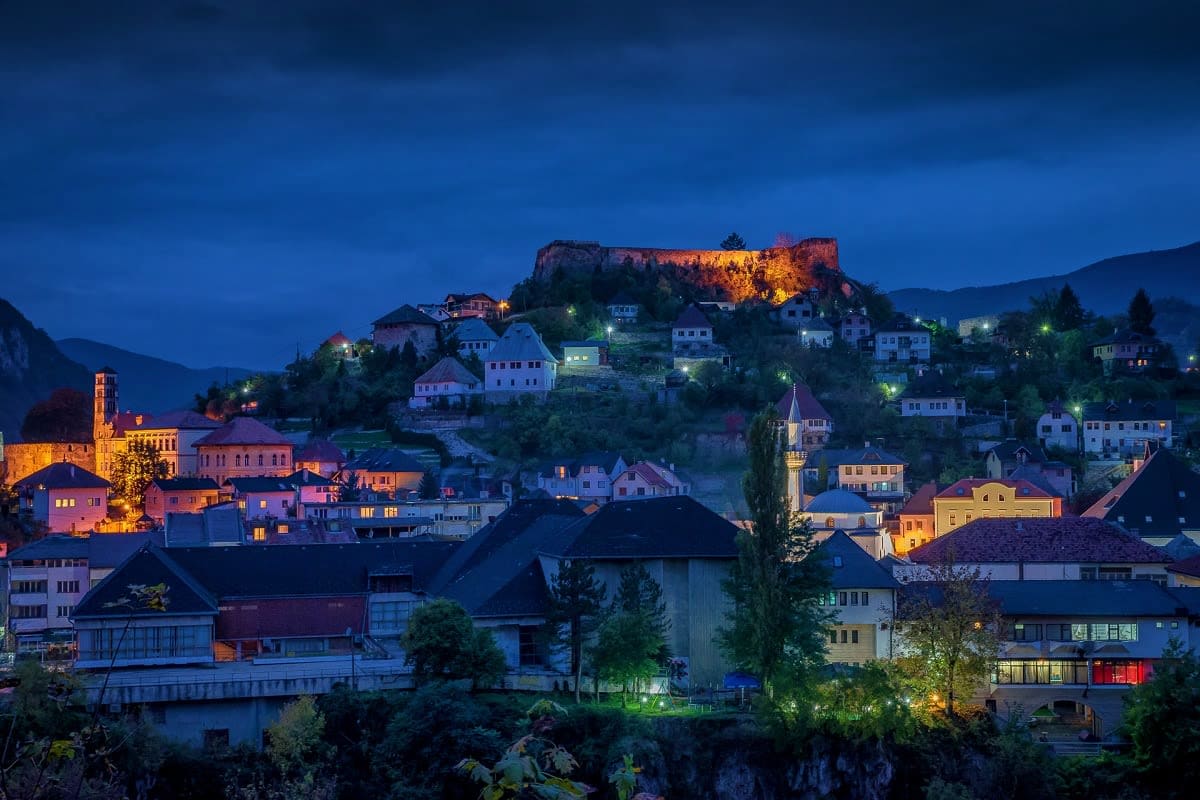 Scenic twilight view of Pocitelj, Bosnia with illuminated medieval fortress on hilltop overlooking traditional stone houses a
