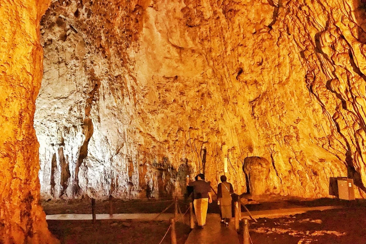 Tourists walking through illuminated cave with golden-orange limestone walls and white mineral deposits, underground cavern e