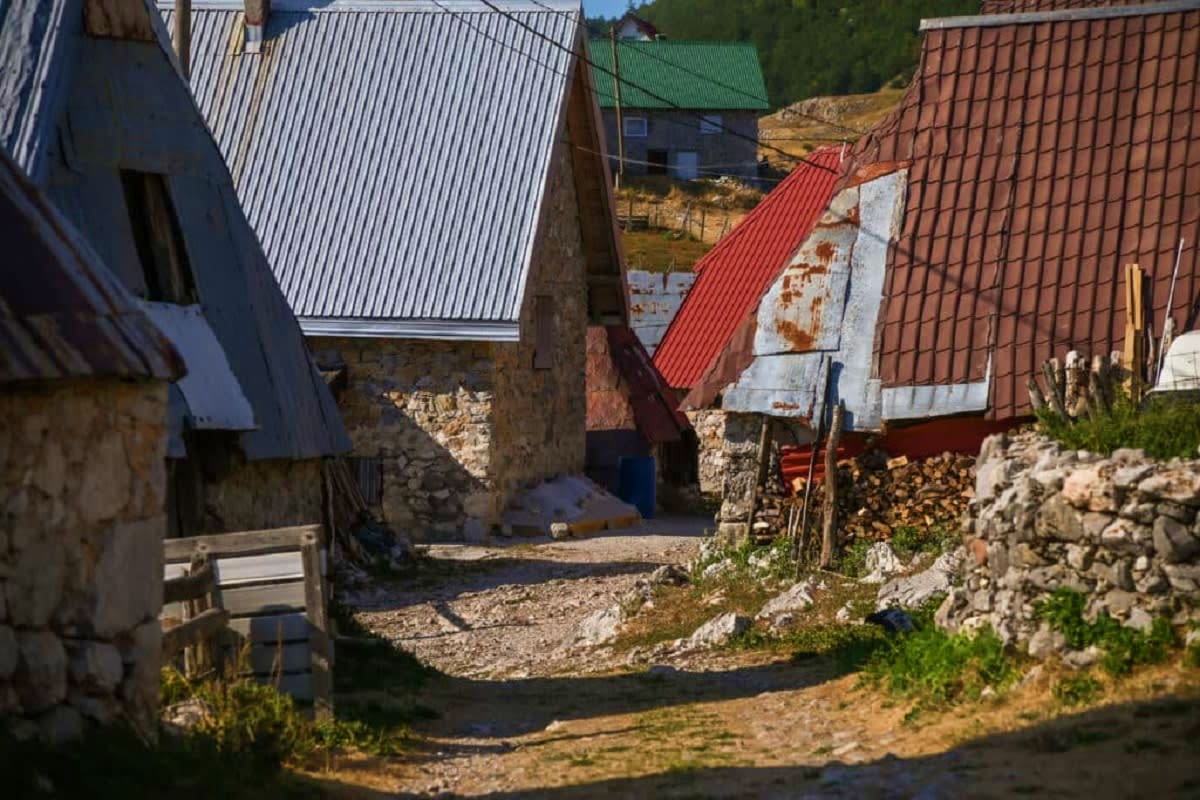Rural village in Bosnia with stone houses featuring corrugated metal roofs in silver, red, and brown, surrounded by rocky ter