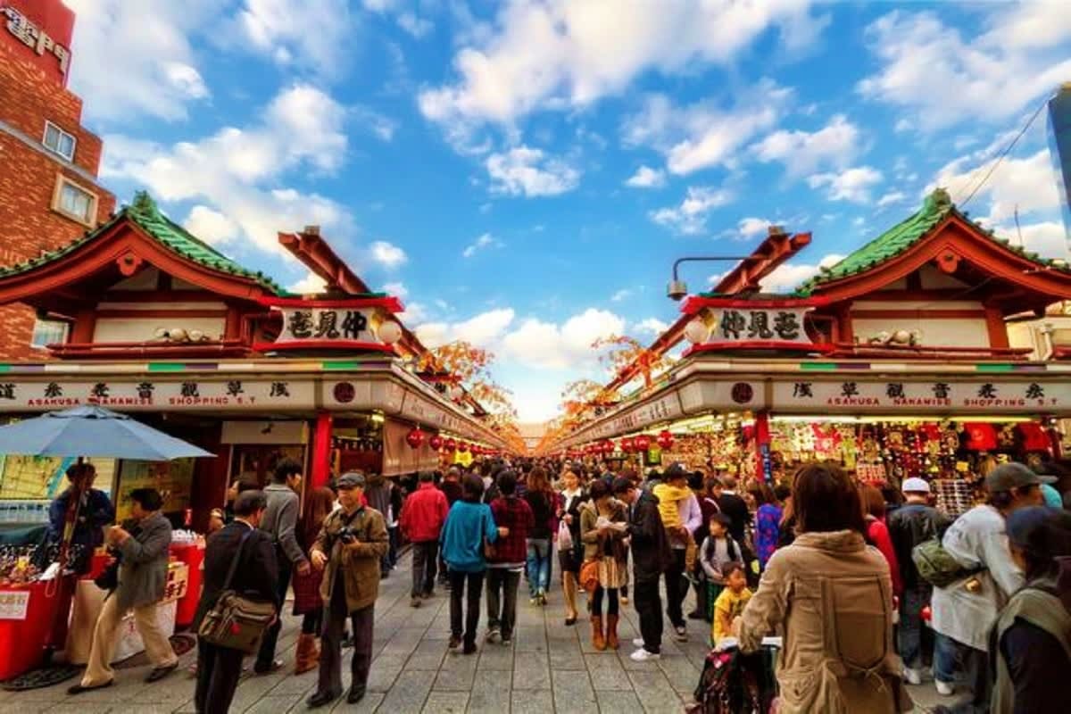 Crowded Asakusa shopping street in Tokyo with red traditional Japanese temple gates and lanterns under blue sky