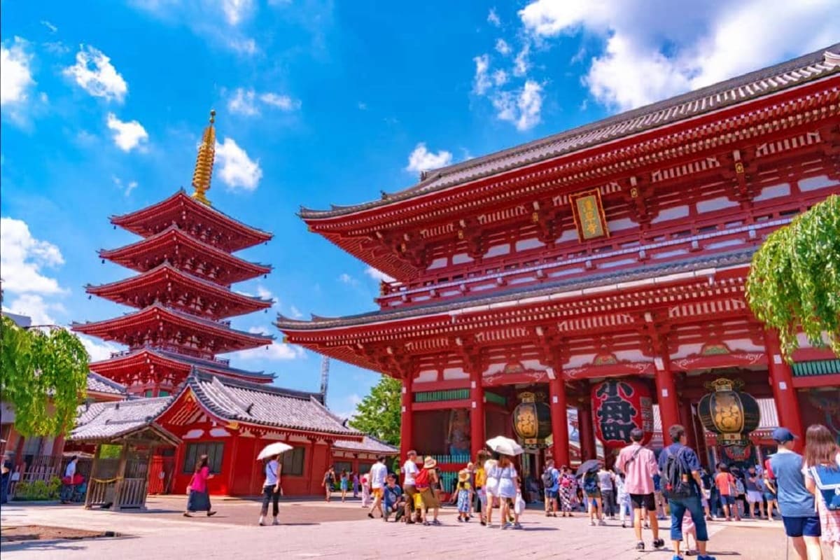 Senso-ji Temple in Tokyo with red pagoda tower, traditional architecture, and tourists in courtyard under blue sky