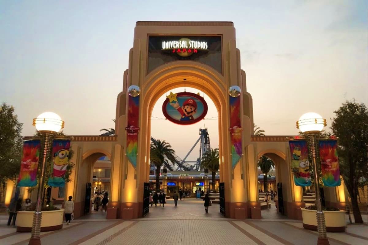 Universal Studios Japan entrance gate illuminated at dusk with Mario character logo and Minion banners, park visitors walking