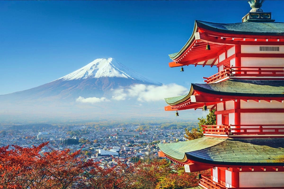 Red Japanese pagoda with Mount Fuji snow-capped peak and city landscape in background during autumn