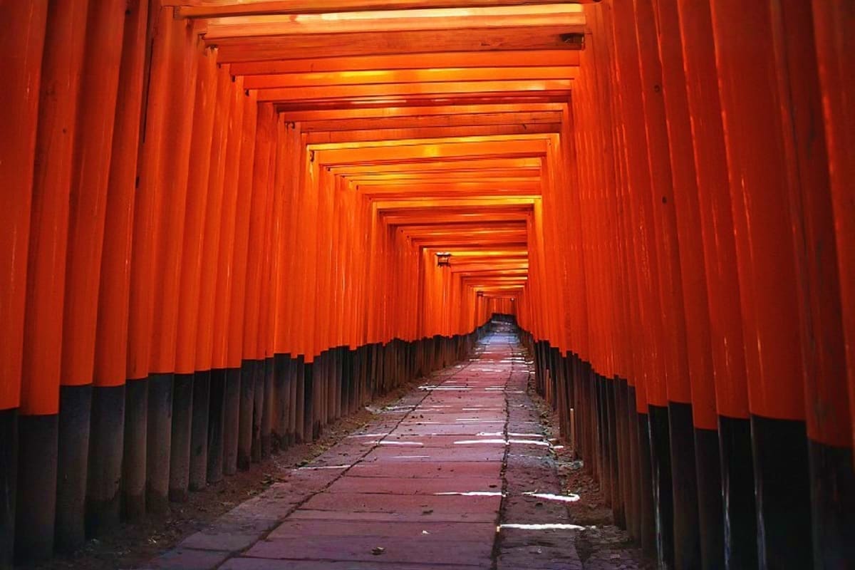 Long tunnel of thousands of bright red torii gates at Fushimi Inari Shrine in Kyoto, Japan, with stone pathway leading throug