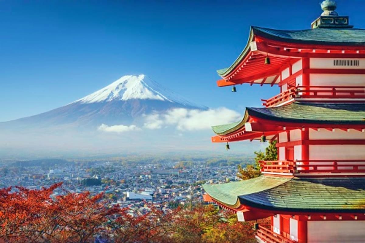 Red Japanese pagoda with snow-capped Mount Fuji and city skyline in the background under clear blue sky