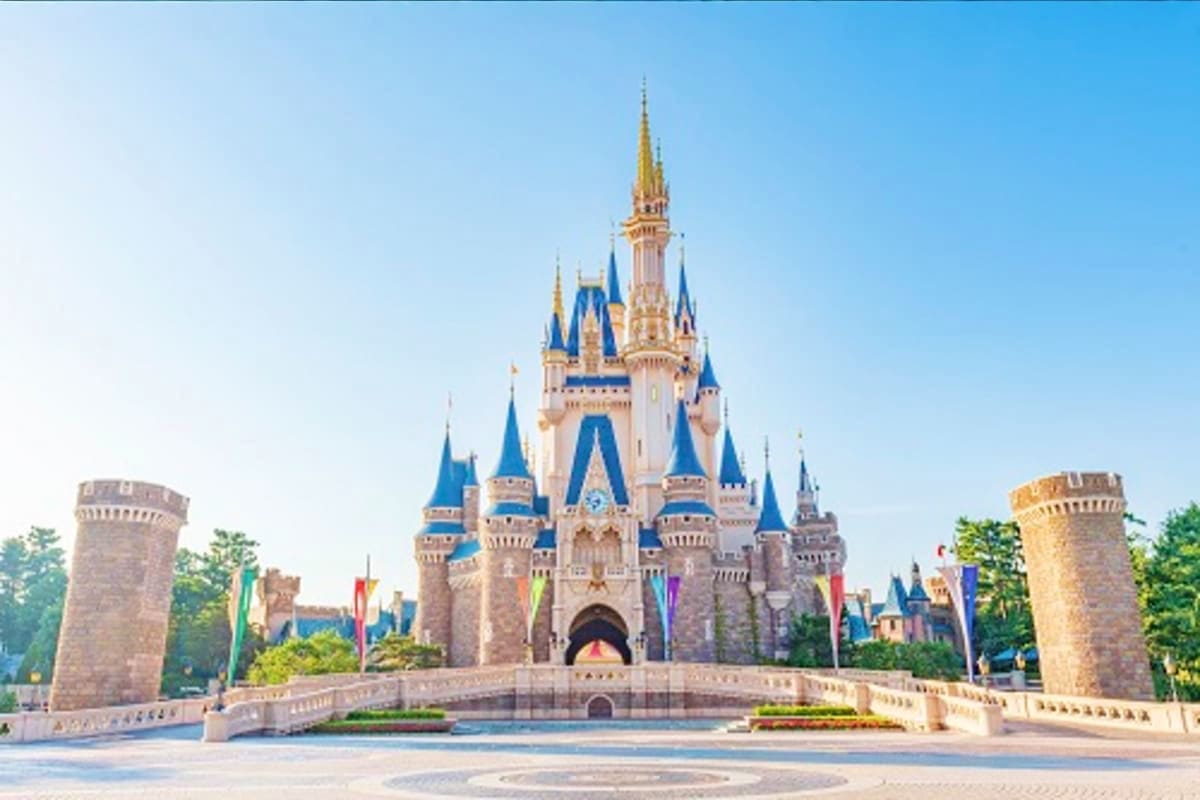 Cinderella Castle at Disney's Magic Kingdom theme park with blue spires, gold towers, and stone bridge under clear sky