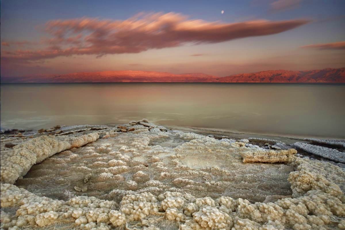 Salt crystalline formations on Dead Sea shore at sunset with Jordanian mountains in background