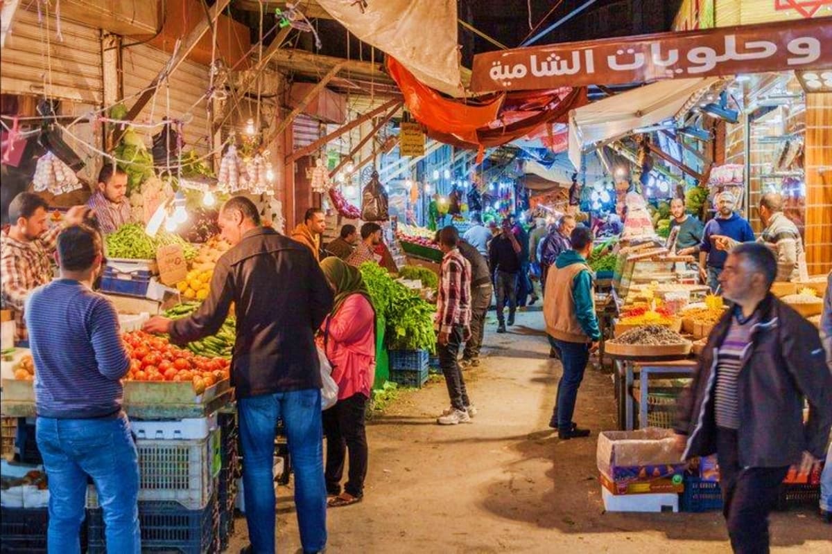 Busy night market in Amman, Jordan with vendors selling fresh produce and shoppers browsing colorful vegetables and fruits un