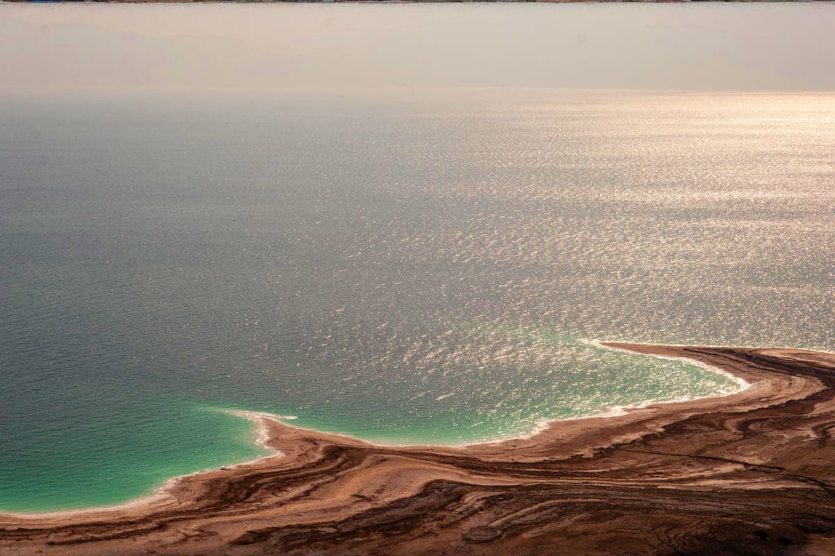 Aerial view of the Dead Sea coastline showing turquoise water, mineral-rich shores, and desert landscape in Jordan.