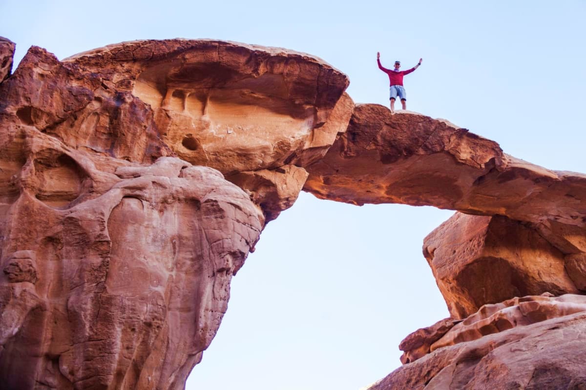 Person celebrating on natural rock arch formation in Wadi Rum desert, Jordan with arms raised