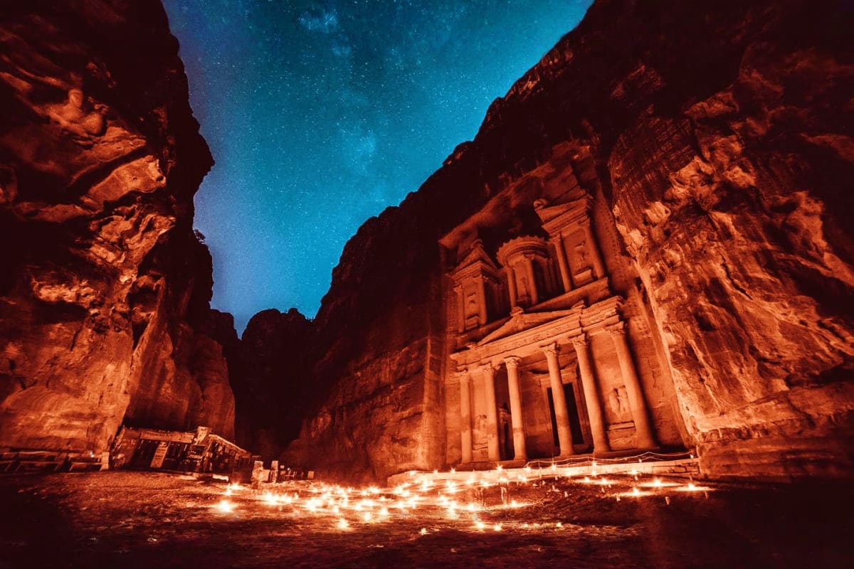 The Treasury monument in Petra, Jordan illuminated at night with candlelights and starry sky above, framed by towering canyon