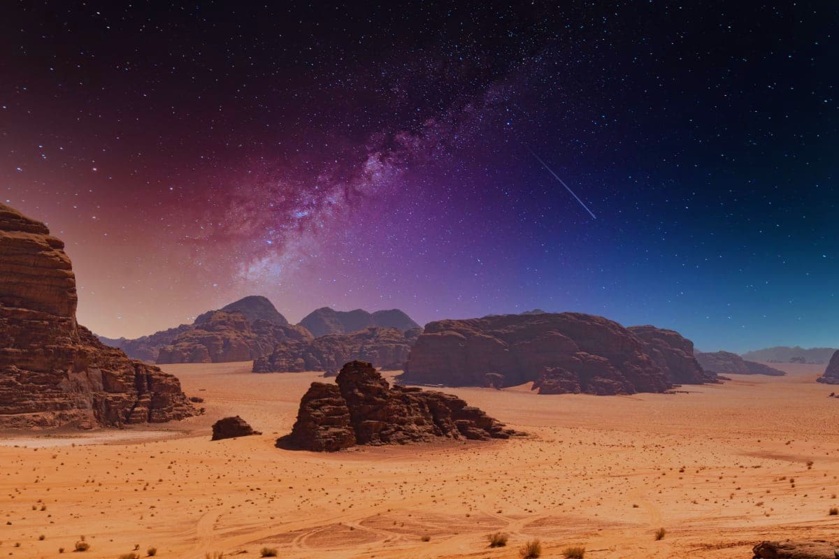 Milky Way galaxy stretching across night sky above desert landscape with rocky sandstone formations in Wadi Rum, Jordan