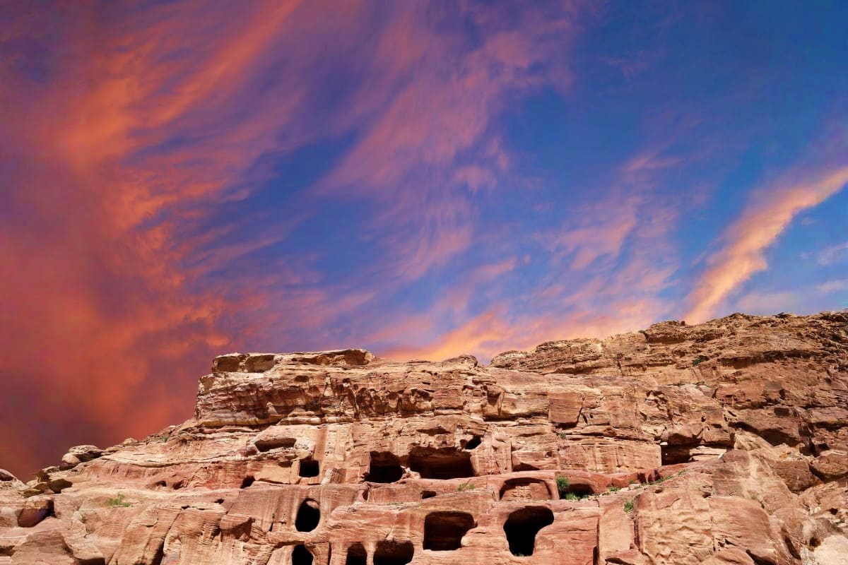 Ancient carved sandstone cliff dwellings at Petra, Jordan with dramatic sunset sky and golden clouds overhead