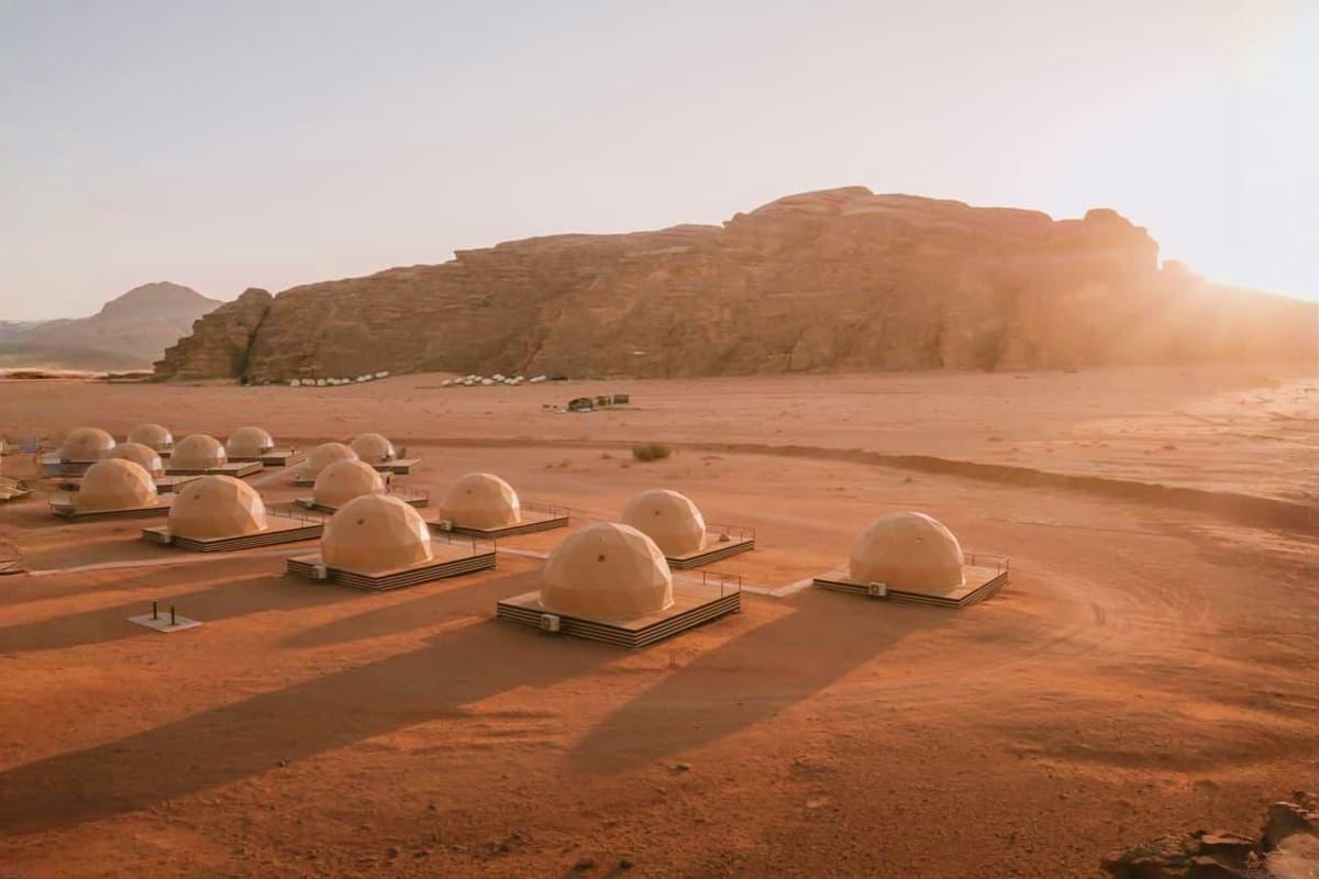 Luxury geodesic dome accommodations on red sand desert with massive sandstone rock formation at sunset in Wadi Rum, Jordan