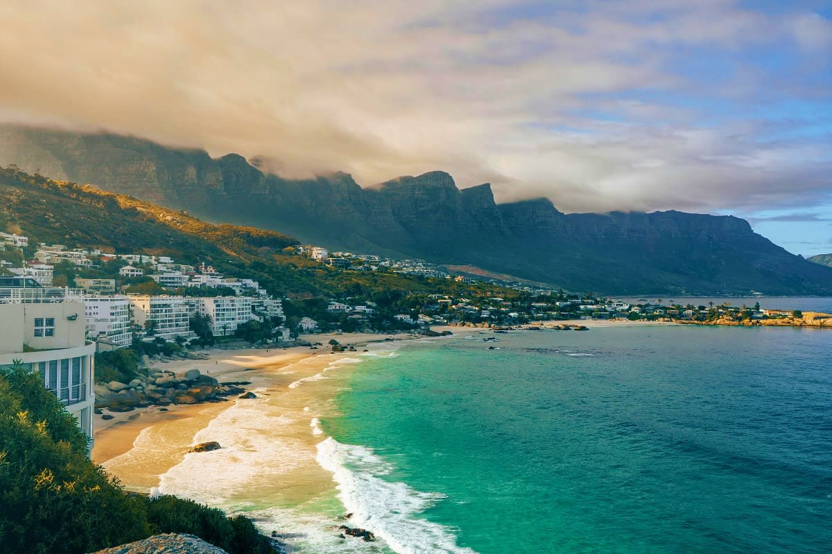 Coastal view of Cape Town with Table Mountain in background, sandy beach with turquoise waters, and residential buildings nes