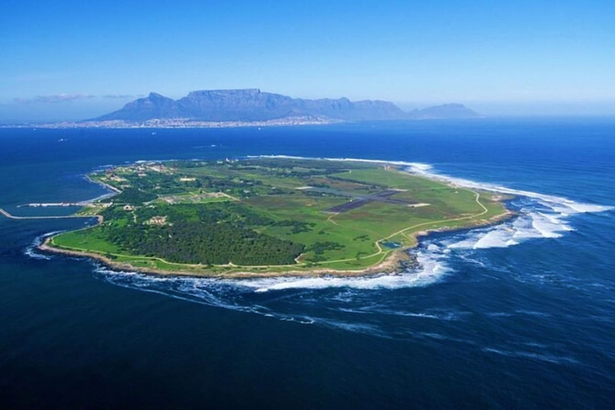 Aerial view of Robben Island with Table Mountain and Cape Town skyline in the background across blue ocean waters