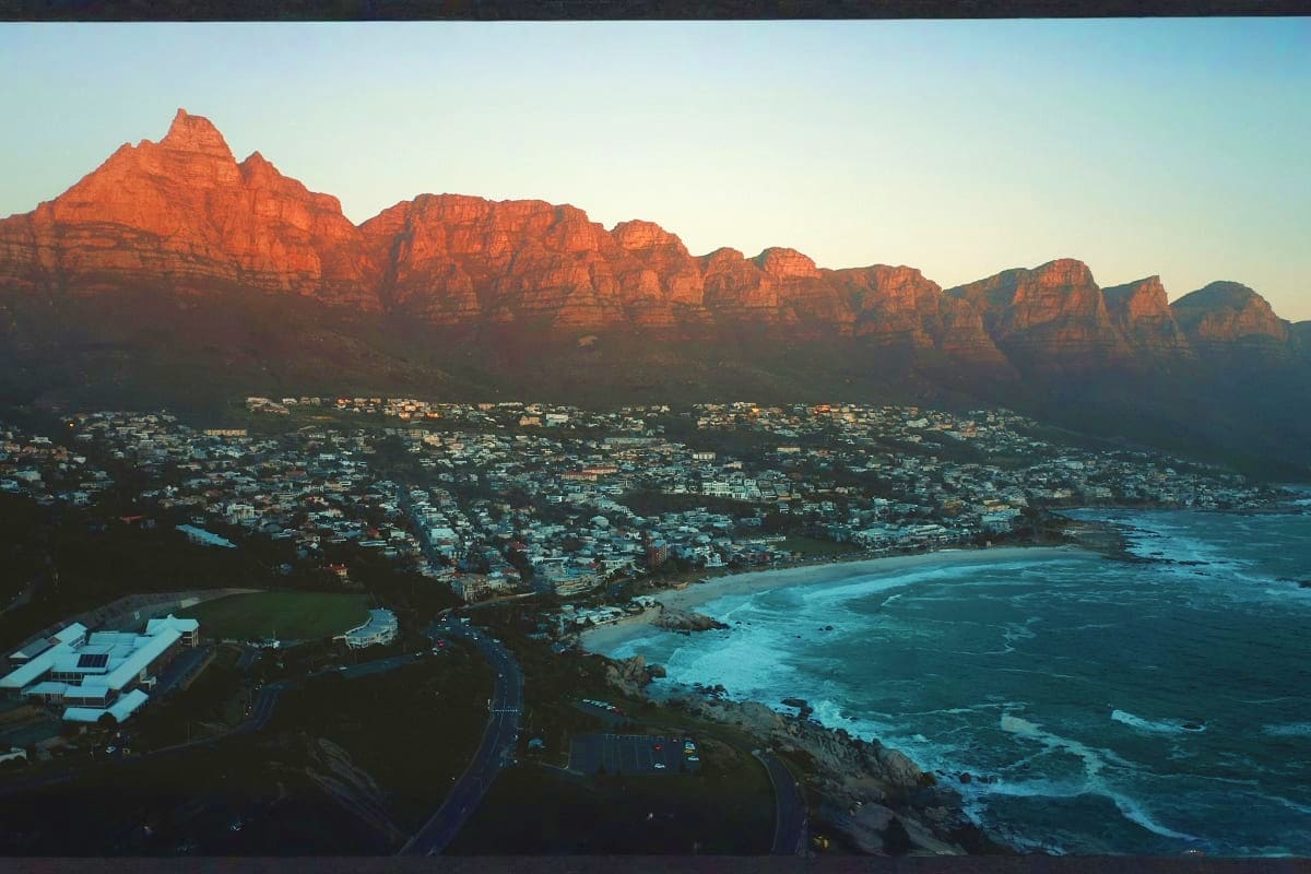 Aerial view of Camps Bay beach with Twelve Apostles mountain range at sunset, Cape Town coastline with turquoise waters and r