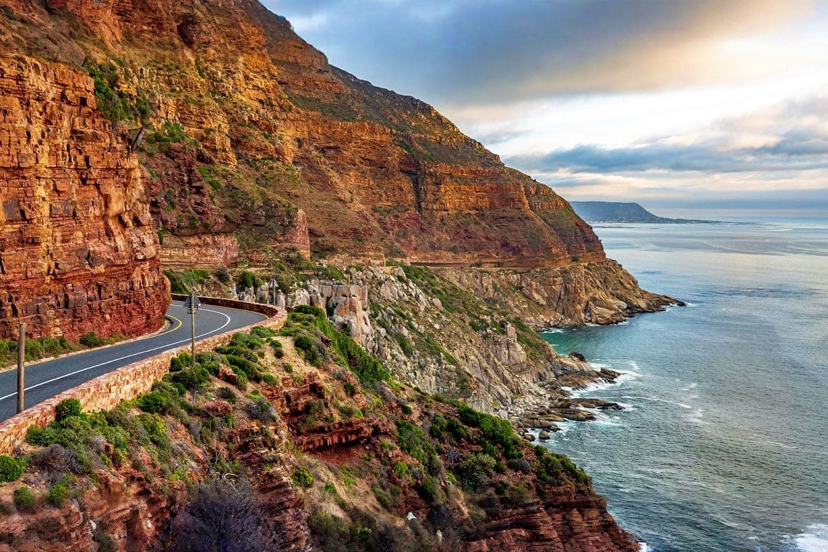 Scenic coastal road winding along red sandstone cliffs above the ocean near Cape Town, South Africa
