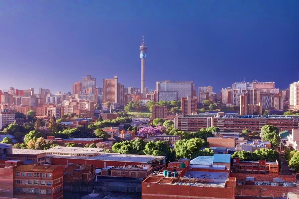 Johannesburg skyline with Telkom Tower and downtown cityscape at dusk, surrounded by green trees and residential buildings