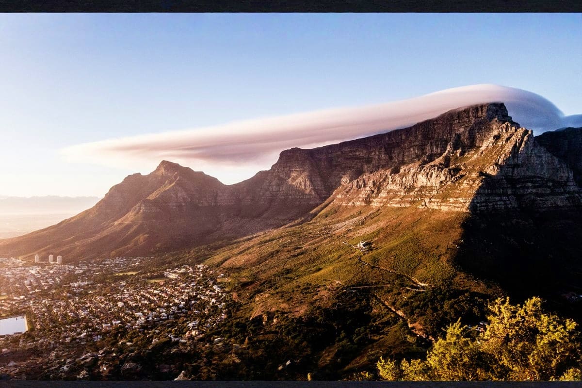 Table Mountain with lenticular cloud formation and Cape Town cityscape below at sunset in South Africa