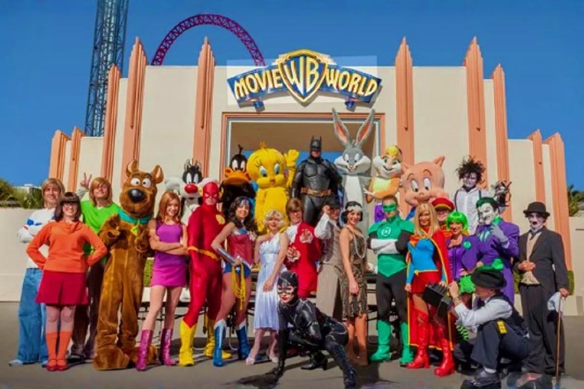 Movie World theme park entrance with costumed characters and superheroes posing in front of iconic Movie World sign and rolle