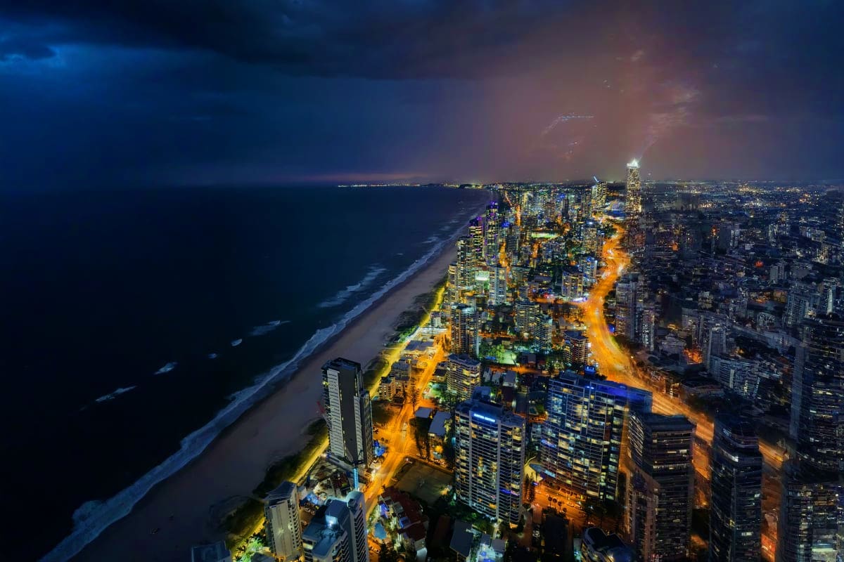 Aerial night view of Gold Coast cityscape with illuminated high-rise buildings, beachfront, and ocean waves along the Austral
