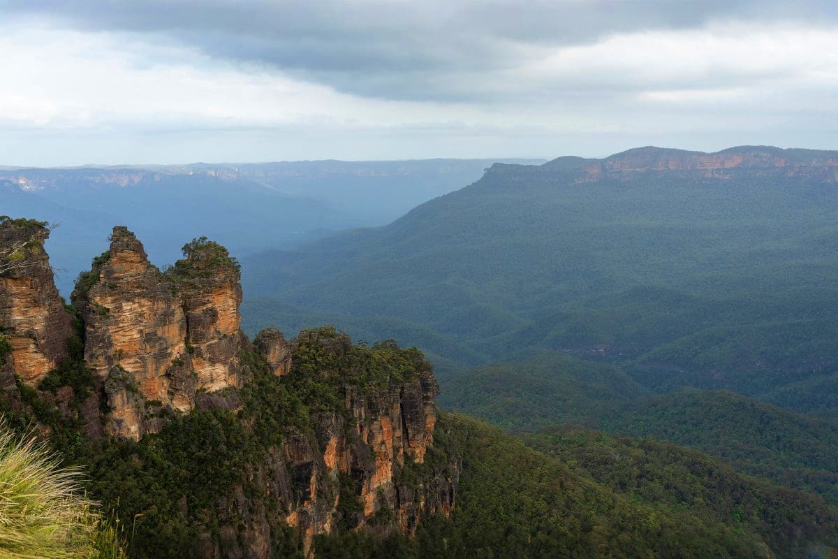 Three Sisters rock formation towering above lush green valleys in Blue Mountains National Park, Australia