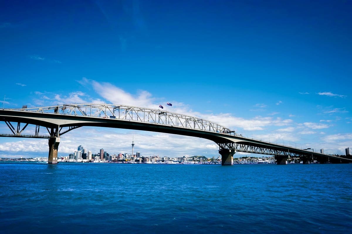 Auckland Harbour Bridge spanning blue water with city skyline and Sky Tower visible in background under clear sky