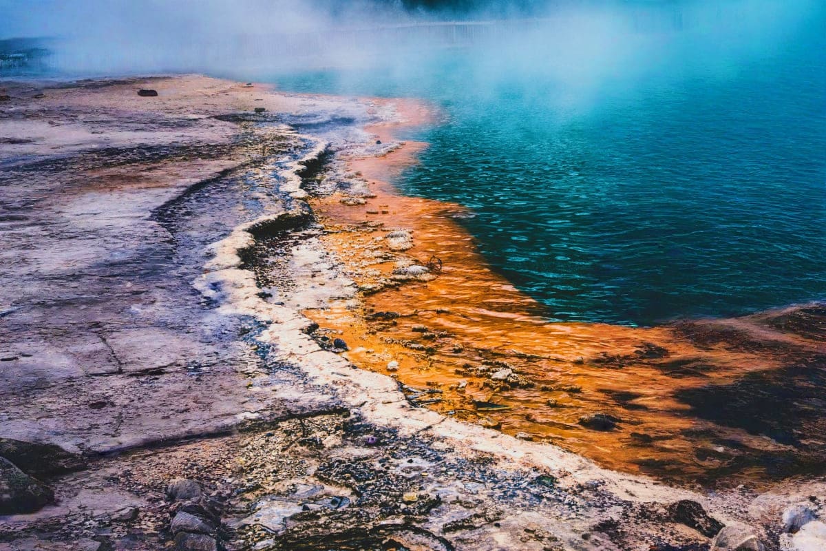 Grand Prismatic Spring in Yellowstone with vibrant turquoise water, orange mineral deposits, and steam rising from geothermal