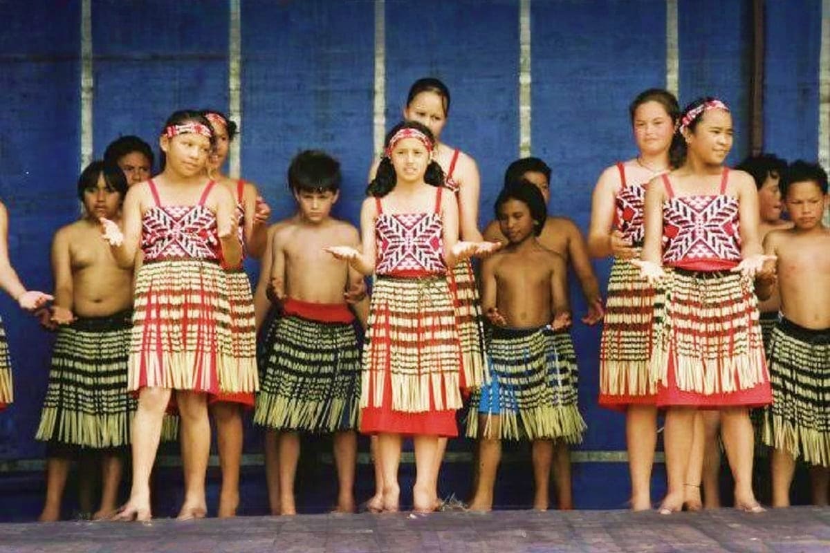 Group of children wearing traditional Maori clothing with geometric patterns and headbands performing cultural dance in New Z