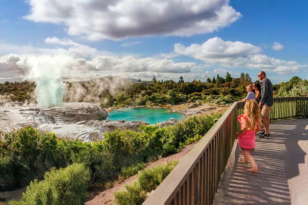 Family viewing geothermal geyser and turquoise hot spring pool from wooden viewing platform in Rotorua, New Zealand